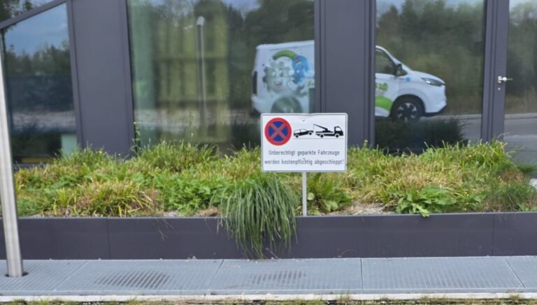 ein Firmentransporter der Hausmeisterfirma fix und fertig spiegelt sich in einer Glasfassade hinter einem Schild parken verboten